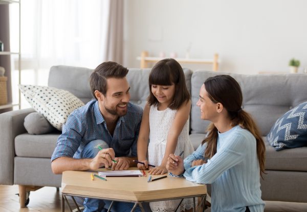 Happy family with kid playing together, caring mom and dad smiling teaching little daughter to draw with color pencils, mother and father having fun with cute child help in creative weekend activity